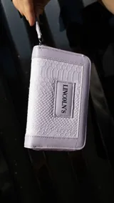 Billetera mediana con textura tipo croco, color mostaza, con cierre perimetral y placa metálica con logo de la marca en el frente.