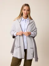 Poncho abierto de tejido de punto en color gris claro con bordes y detalles de bolsillos en gris oscuro. Presenta un diseño holgado y versátil con placa metálica decorativa en uno de los bolsillos frontales.