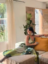 Vestido largo verde con diseño estampado tipo tie-dye y detalles dorados, de corte fluido, un solo hombro y diseño amplio.