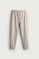 Pantalón jogger color beige de tejido transpirable y elástico con cintura elástica ajustable con cordón, bolsillos frontales y bajo con vuelta.