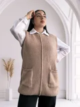 Chaleco largo de punto color beige, con cuello redondo y bolsillos frontales. Diseño sin mangas y corte recto.