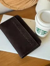 Billetera de cuero marrón con cierre de cremallera y diseño trenzado en el frente. Cuenta con múltiples compartimentos internos para tarjetas y billetes.