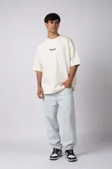 Remera negra de corte oversize confeccionada en tela pesada. Presenta un bordado frontal con la palabra 'REWIND' y un diseño de parche en la espalda con estética de papel roto.