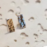 Par de caravanas rectangulares de plata 925 con textura irregular. Una caravana es color dorado y la otra es color celeste.