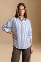 Camisa de algodón de corte holgado y diseño a rayas verticales en color celeste y blanco, con cuello camisero, cierre frontal de botones, bolsillo aplicado en el pecho y mangas largas con puños abotonados.