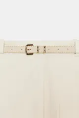Falda midi de tiro medio color beige, con pliegues en la parte delantera, abertura frontal en el bajo y cinturón combinado a tono con hebilla metálica.