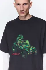 Remera oversized negra de punto de algodón pesado, con cuello redondo acanalado, hombros caídos, mangas cortas y estampa frontal de la banda Gorillaz en un vehículo militar con detalles en verde.
