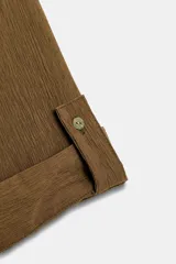 Camisa negra de textura arrugada, con cuello solapa, escote en V y cierre frontal de botones. Cuenta con mangas cortas terminadas en vuelta con trabilla y botón.