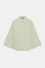 Camisa de corte oversize en color verde claro, con cuello solapa, cierre frontal de botones y mangas anchas de largo tres cuartos. Presenta un bolsillo de plastrón en el pecho.