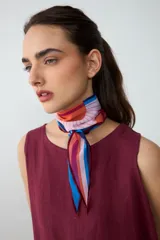 Pañuelo liviano y translúcido de forma romboidal, con diseño estampado inspirado en un atardecer, en tonos naranja, bordó, rosa y azul.