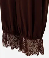 Pantalón bloomer marrón de cintura alta, confeccionado en viscosa con textura crinkle. Cuenta con un diseño amplio y cómodo, perneras voluminosas, puños con elástico interno y aplicación de encaje floral en los puños.