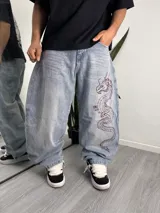 Pantalón jean baggy de corte holgado y tiro medio, en tono celeste claro con efecto desteñido. Presenta un bordado de dragón en color rojo oscuro en la pierna izquierda.