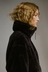 Abrigo de corte oversized confeccionado en tejido de efecto piel sintética suave. Presenta cuello elevado, cierre frontal con cremallera, hombros caídos, costuras visibles en los codos y bolsillos laterales al bies. Incluye forro interior.