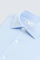 Camisa de manga larga, color celeste con finas rayas verticales blancas, cuello italiano y cierre frontal de botones.