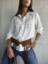 Camisa blanca de corte clásico con cuello camisero, mangas largas y detalle de bordado geométrico en el panel frontal superior. Confeccionada en tela liviana con textura.