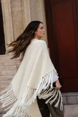 Poncho triangular de lana en color crudo, con diseño de tejido texturizado y terminaciones de flecos largos en todo el borde.