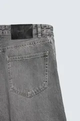 Jeans de denim de algodón en color negro con efecto lavado, corte amplio y silueta curva tipo barrel fit con pinzas en las rodillas. Presenta diseño clásico de cinco bolsillos y cierre frontal con cremallera y botón metálico.