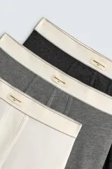 Pack de tres bóxers de hombre en tonos neutros: blanco, gris medio y gris oscuro. Tienen tejido elástico con acabado suave y cintura elástica ancha de color crema con etiqueta central.