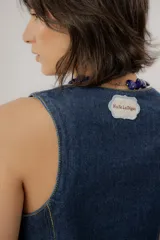 Chaleco de denim azul con cuello en V, cierre frontal con botones metálicos y pespuntes en contraste.