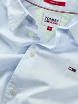 Camisa celeste de manga corta Tommy Hilfiger, confeccionada en algodón orgánico y nylon. Tiene cuello clásico, cierre frontal con botones, dobladillo curvo y logo bordado en el pecho.