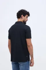 Chomba de piqué en color negro, de manga corta, con cuello y puños tejidos con líneas a contraste. Presenta cierre frontal parcial con botones y pequeño logo bordado en el pecho.