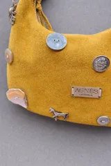 Cartera baguette color naranja con correa corta para llevar al hombro. Decorada con tachas, botones y dijes.