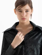 Camisa de jacquard con diseño de flores sutiles, color blanco, con cuello amplio de puntas marcadas, mangas largas con puños y cierre frontal con botones.