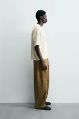 Camiseta de manga corta y cuello redondo, color crema o blanco roto, con un parche texturizado en el pecho que simula barras verticales.