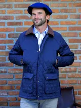 Campera de hombre con diseño capitoneado en color azul, cuello de pana en tono marrón, cierre frontal con cremallera y botones a presión, y dos bolsillos frontales con solapa.