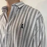 Camisa de manga larga con diseño de rayas verticales en tonos azul y blanco, cuello clásico y cierre frontal con botones.