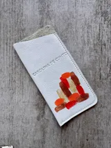 Portalentes Carolina De Cunto modelo Aruba, confeccionado en cuero blanco con diseño pintado a mano de formas geométricas en tonos corales, marrones y amarillos. Incluye logo de la marca grabado.