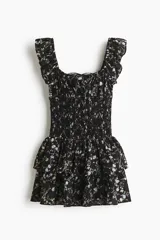 Vestido corto negro con estampado floreado, escote cuadrado con volados en los tirantes, cuerpo fruncido tipo nido de abeja y falda de capas escalonadas.