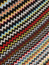 Chal o bufanda de tacto suave con diseño de zigzag (chevron) multicolor sobre fondo beige. Presenta flecos en los extremos.