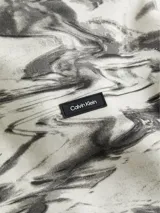 Buzo con capucha Calvin Klein confeccionado en mezcla de algodón y poliéster con estampado abstracto en tonos grises. Presenta cuello con capucha, puños y dobladillo de punto canalé, bolsillo de canguro y logo de Calvin Klein en la parte delantera.