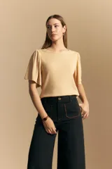Remera de rib color beige, con cuello redondo y mangas cortas amplias con leve frunce en los hombros. Confeccionada en tejido elastizado de textura acanalada.
