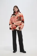 Buzo de polar tipo canguro con cuello alto y cierre frontal parcial. Presenta un diseño estampado con bloques de colores en tonos rosado, naranja, marrón y crema, y cuenta con un bolsillo frontal con cierre en contraste de color marrón.