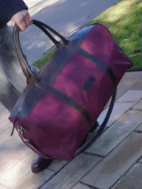 Bolso sport de lona color bordó en formato XL, con detalles y asas de cuero marrón. Cuenta con cierre principal y correa para llevar al hombro.