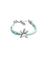 Pulsera de diseño náutico con hilo de seda color turquesa, intercalado con cuentas metálicas plateadas y cristales facetados en tono azul. Presenta un dije central en forma de estrella de mar plateada y cierre de mosquetón con placa de marca.