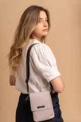 Phonebag pequeña color mostaza, confeccionada en cuero sintético, con solapa frontal y correa ajustable con logo de la marca.