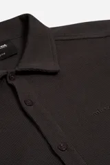 Camisa de manga larga confeccionada en tejido tipo waffle, con cuello clásico y botonadura frontal. Presenta una textura distintiva y estructura liviana.