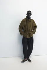 Parka amplia de Zara Woman Collection confeccionada en hilatura con mezcla de algodón, en color verde militar. Presenta cuello alto, manga larga con trabillas y botón, bolsillos laterales ocultos en costura, cintura ajustable con cordones y cierre frontal con botones.