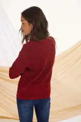Buzo de tejido de punto calado en color rojo, con cuello redondo y mangas largas. Presenta un diseño con texturas variadas en el tejido.