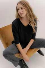 Buzo básico de lambswool color gris oscuro, con escote en V y mangas 3/4. Presenta un fit amplio y tajos laterales. Los puños tienen un detalle de ribete en color celeste y amarillo.