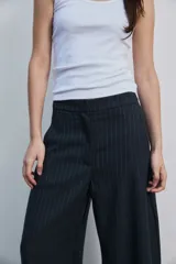 Pantalón de vestir de corte ancho y relajado, color negro con sutiles rayas diplomáticas verticales. Presenta bolsillos laterales y cierre frontal oculto.