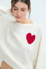 Sweater de punto gris con diseño de corazón blanco en el pecho, cuello redondo y mangas largas.
