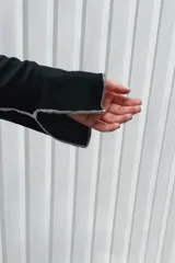 Remera de manga larga color negro, con cuello redondo y diseño de costuras verticales expuestas en color blanco que recorren el frente y las mangas.