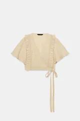 Top crop de escote en pico y manga corta con volados. Presenta un diseño cruzado que se ajusta mediante una lazada lateral y cuenta con una textura de cuadrícula sutil en toda la prenda.