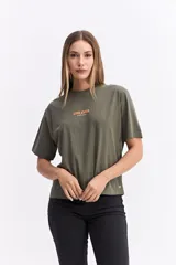 Remera de algodón color verde oliva, con corte relajado y manga corta. Presenta una estampa gráfica grande en la espalda con motivos florales abstractos y texto.