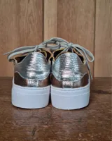 Zapatilla urbana de cuero con diseño combinado en color dorado metalizado y gamuza en tono tostado. Presenta cordones al tono, suela de goma blanca y detalles en cuero marrón en la parte posterior.