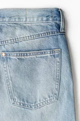Jean de cinco bolsillos en denim de algodón rígido, tiro alto, con cierre y botón. Corte estándar con pierna acampanada amplia. Presenta un lavado celeste claro con efecto degradado o tie-dye en la parte inferior de las piernas.